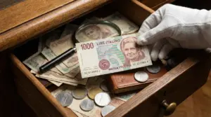 Banconota da 1000 lire con Maria Montessori tenuta da una mano con guanto bianco sopra un cassetto con monete e altre banconote