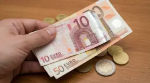 Una mano tiene banconote da 10 e 50 euro sopra un tavolo con monete sparse
