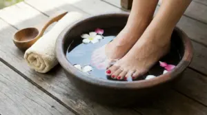 Piedi immersi in una ciotola di acqua con fiori su una superficie in legno