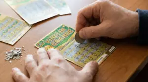 Una persona gratta un biglietto gratta e vinci con una moneta su un tavolo di legno