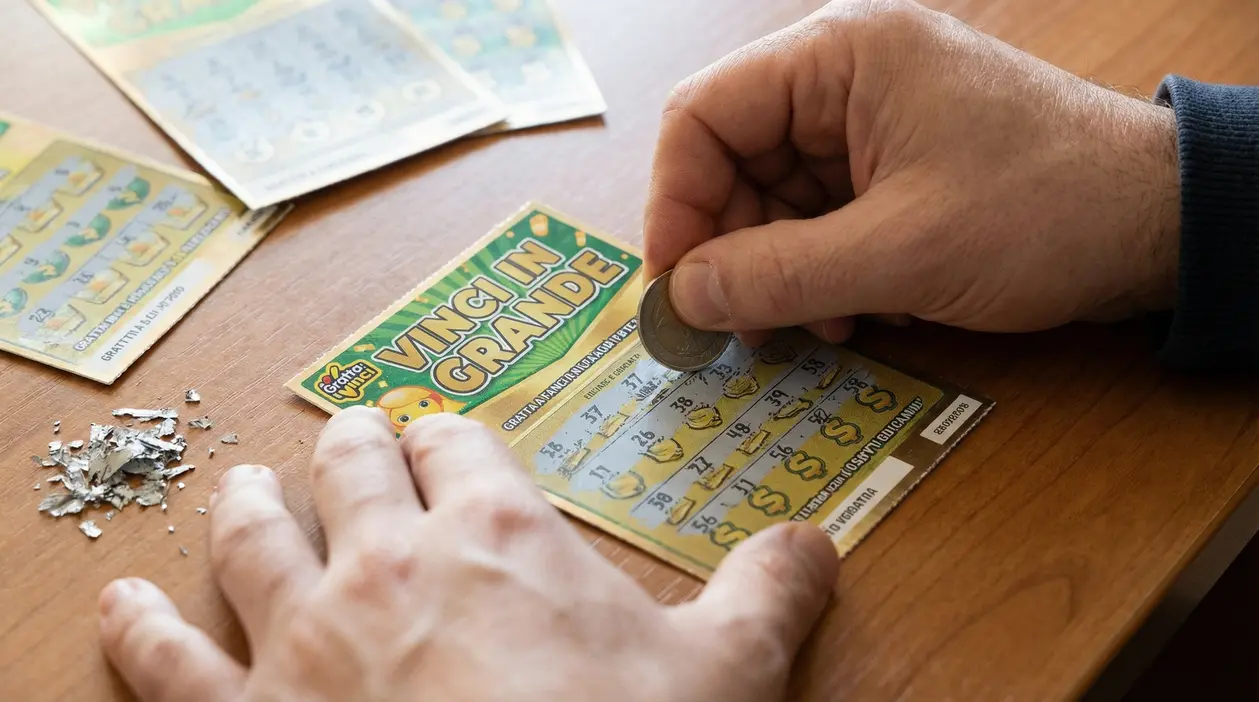Una persona gratta un biglietto gratta e vinci con una moneta su un tavolo di legno