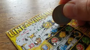 Mano che gratta un biglietto gratta e vinci con una moneta su un tavolo di legno