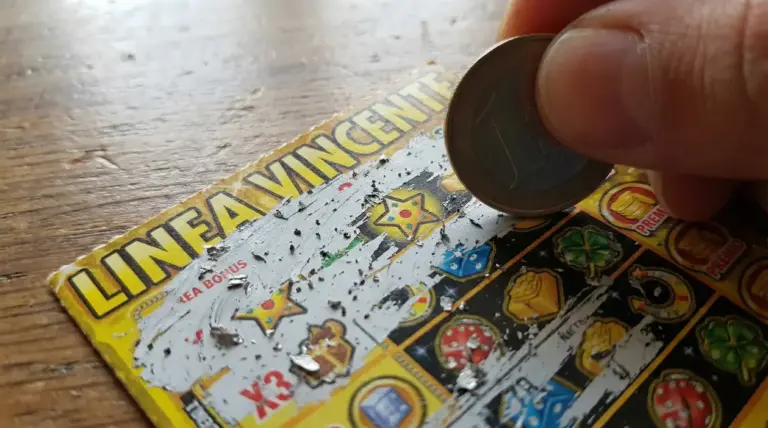 Mano che gratta un biglietto gratta e vinci con una moneta su un tavolo di legno